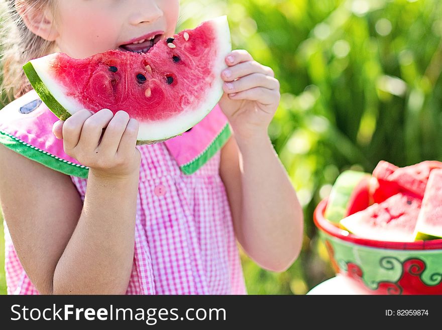 A young girl eating watermelon outdoors in the summer.