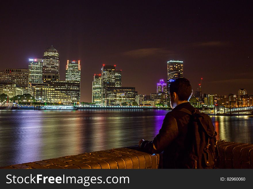 Man standing on banks of River Thames overlooking London, England skyline illuminated at night. Man standing on banks of River Thames overlooking London, England skyline illuminated at night.