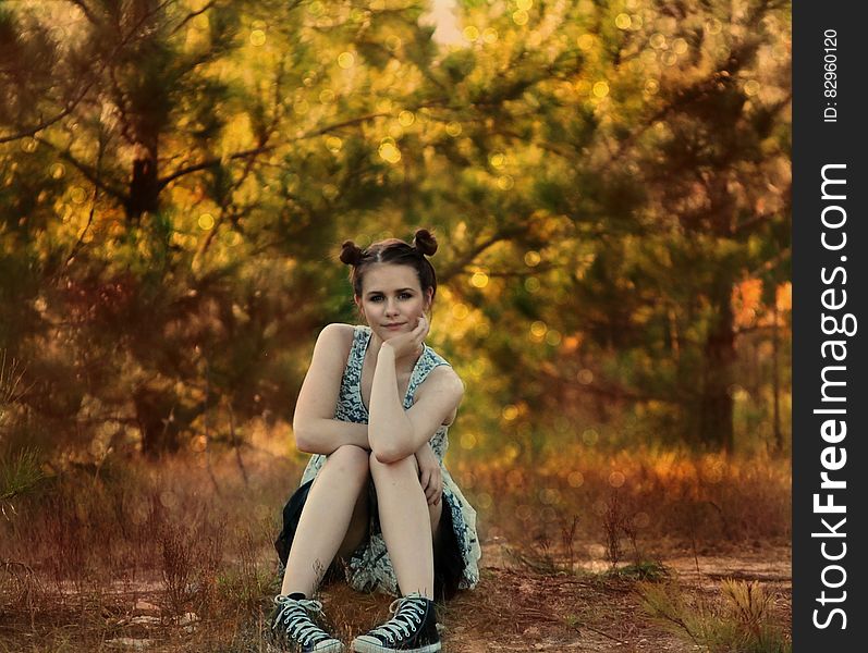 Attractive young woman wearing a black and white patterned dress sitting on the ground with trees in their Autumn colors behind and contemplating the big questions of life. Attractive young woman wearing a black and white patterned dress sitting on the ground with trees in their Autumn colors behind and contemplating the big questions of life.