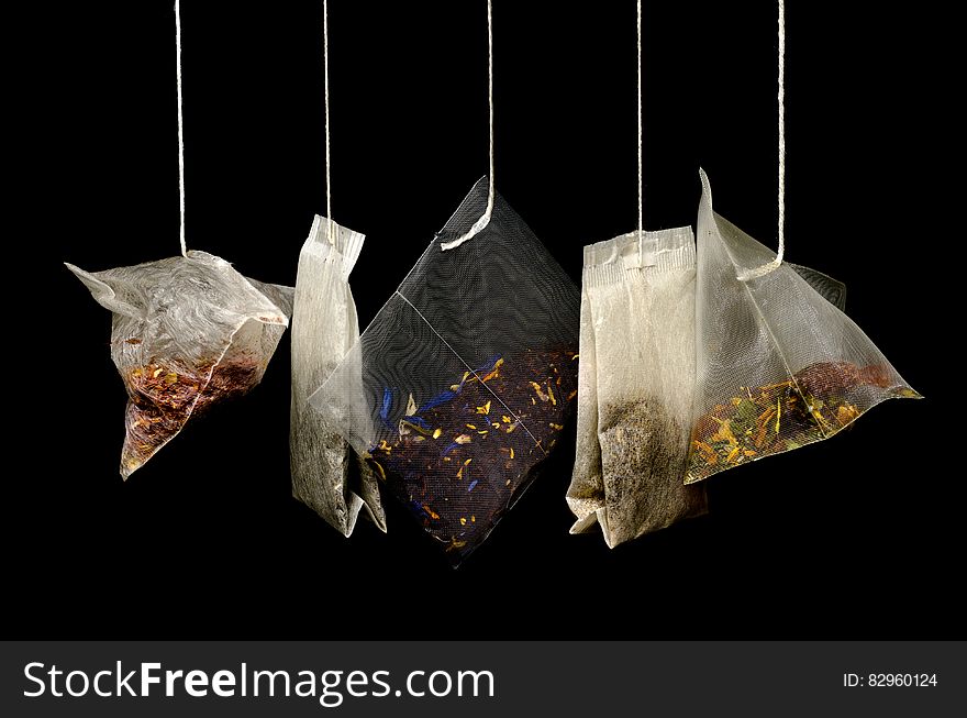 Close up on variety of tea bags hanging against white background.