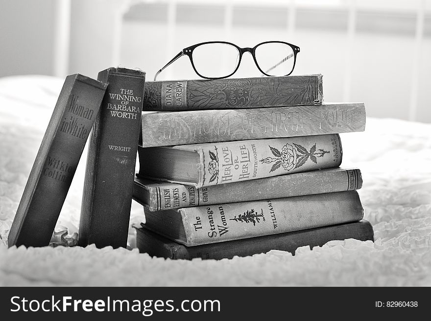 Stack of books on bed with eyeglasses in black and white. Stack of books on bed with eyeglasses in black and white.