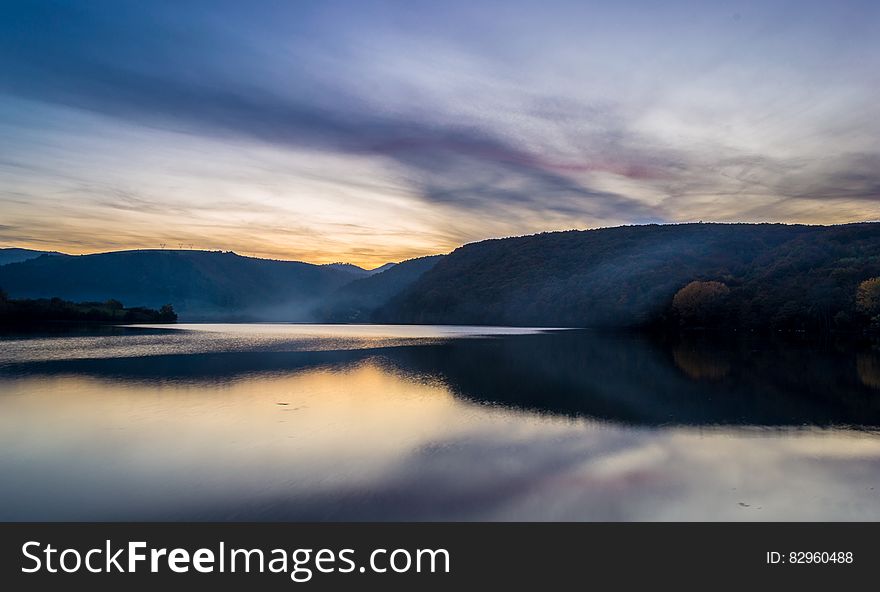 Sunset behind hillside of lakefront landscape with cloudy skies. Sunset behind hillside of lakefront landscape with cloudy skies.