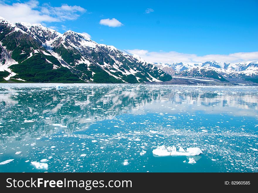 Mountain Filled With Snow Near Calm Sea Under White Clouds And Blue Sky During Daytime