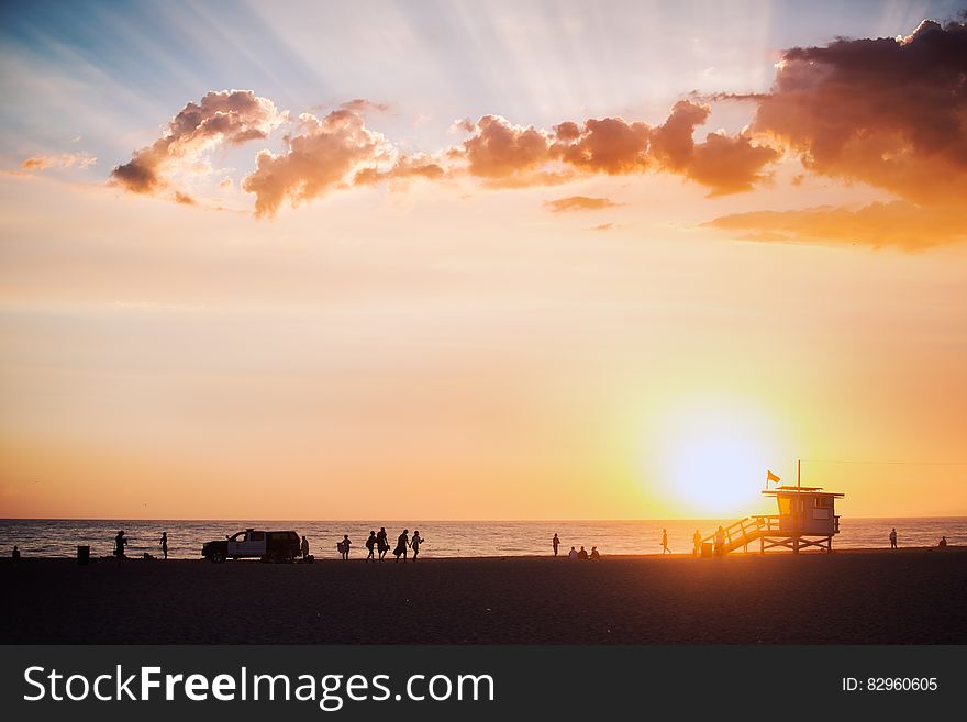 Silhouette of lifeguard shack and people on beach at sunset.