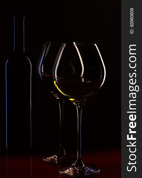 Stemmed wineglasses with red and white wine and bottle on black background. Stemmed wineglasses with red and white wine and bottle on black background.