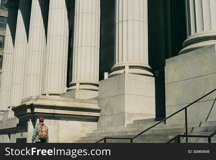 Person walking past large building with classical style stone columns.