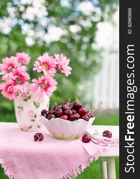 Pink Petaled Flower Beside White And Green Bowl Full Of Cherry