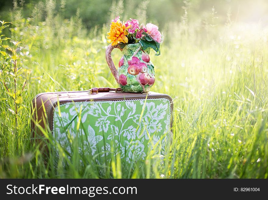 Vase of flowers on decorative suitcase in field of long grass with summer sunlight. Vase of flowers on decorative suitcase in field of long grass with summer sunlight.