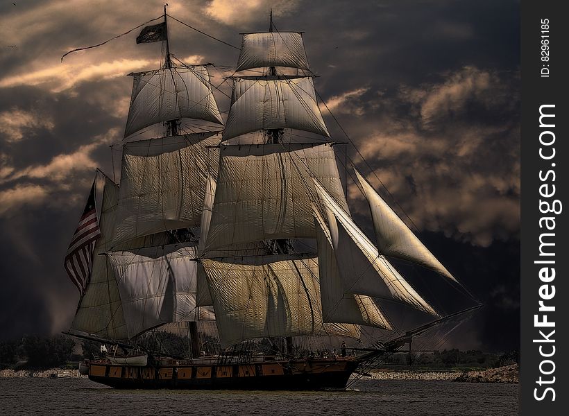 Tall sailing ship in waters along snowy coastline against stormy skies. Tall sailing ship in waters along snowy coastline against stormy skies.