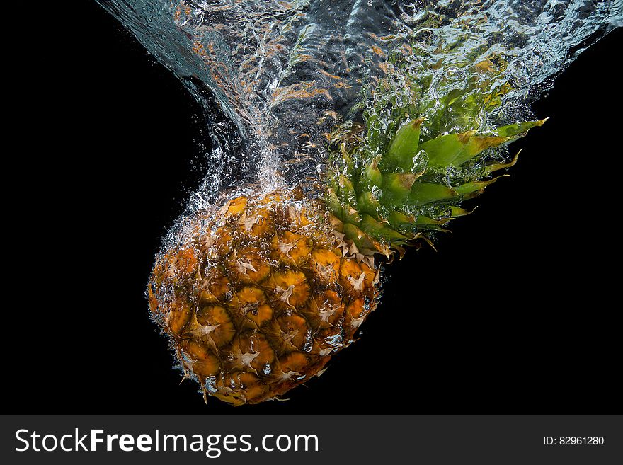 Whole fresh pineapple splashing into water against black background. Whole fresh pineapple splashing into water against black background.