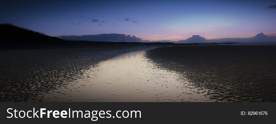 Sunset over country lake with pink and blue skies and mountain peaks.