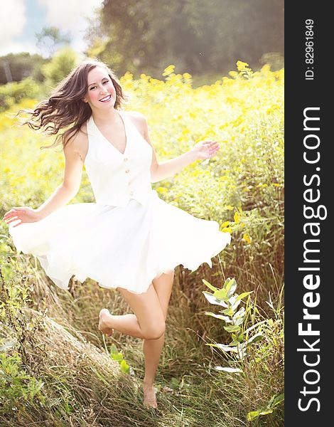 Sunny portrait of long brunette in white dress running barefoot through grassy field. Sunny portrait of long brunette in white dress running barefoot through grassy field.