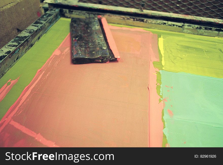 Table with black wooden squeegee and three colors pink yellow and green for generating artistic screen prints in combinations of these colors, studio background. Table with black wooden squeegee and three colors pink yellow and green for generating artistic screen prints in combinations of these colors, studio background.