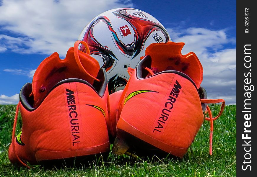 A close up of red soccer boots and a ball on green grass. A close up of red soccer boots and a ball on green grass.