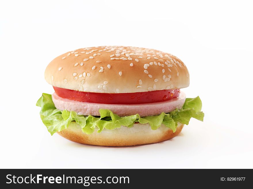 Tasty cheeseburger in a seeded bun with tomato, lettuce, plus cheese and ham, white background.