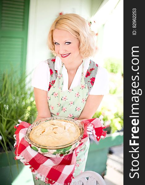 Woman in Pink White Floral Apron Smiling While Holding a White Creme Food during Daytime