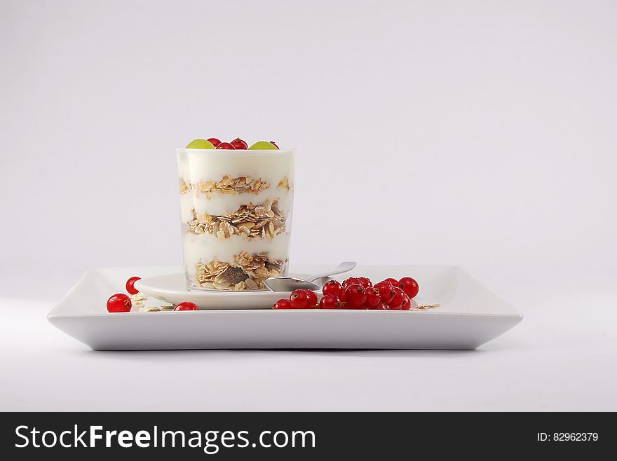 A layered breakfast with yogurt, cereals and berries and fruits in a glass on a rectangular plate.