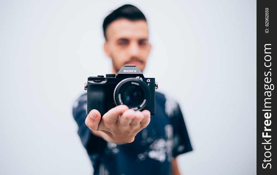 Young man holding a digital camera on palm on hand, focus on camera and white studio background.