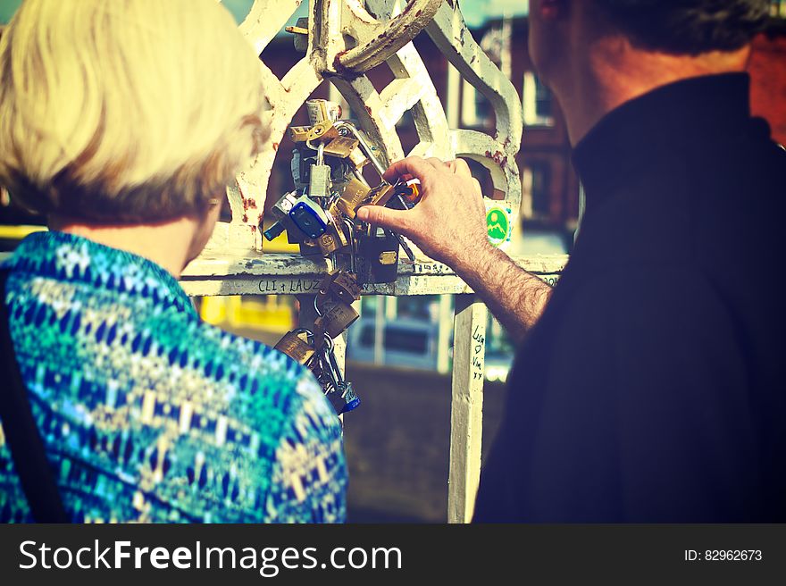 Rear portrait of couple looking at and touching padlocks on outdoor chain, unbreakable love concept. Rear portrait of couple looking at and touching padlocks on outdoor chain, unbreakable love concept.