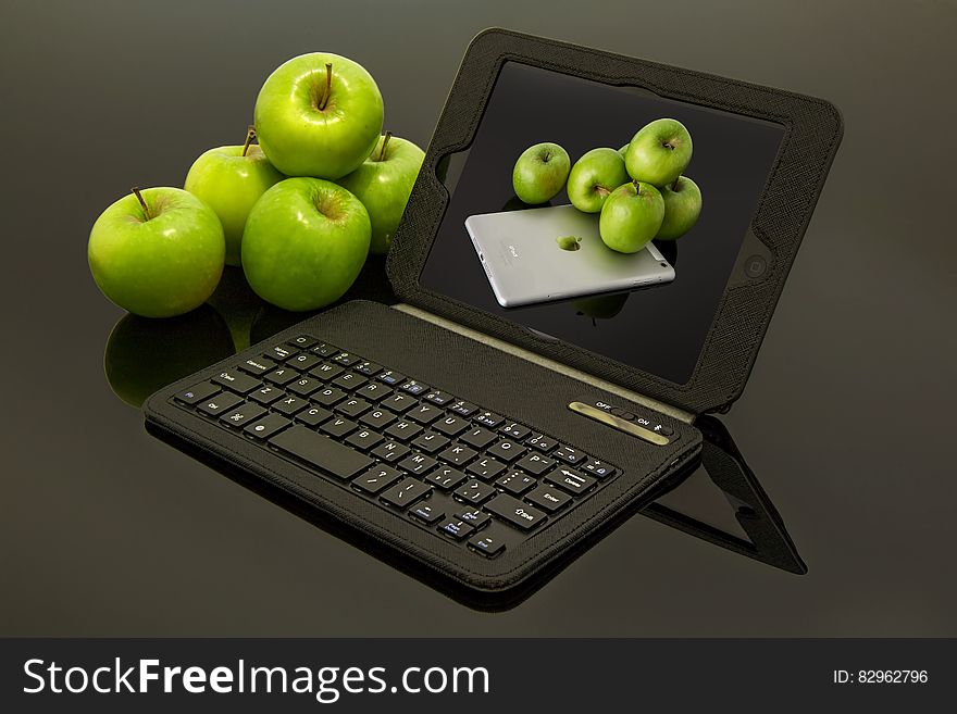 A black laptop with apple desktop background and green apples beside it. A black laptop with apple desktop background and green apples beside it.