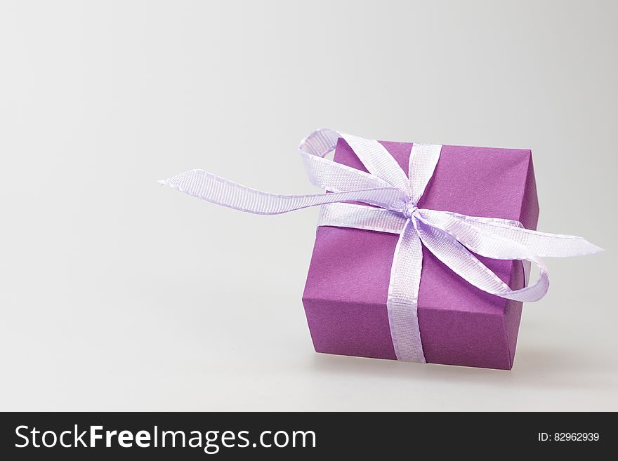 Square shaped present wrapped in purple paper with decorative ribbon, white studio background with copy space. Square shaped present wrapped in purple paper with decorative ribbon, white studio background with copy space.