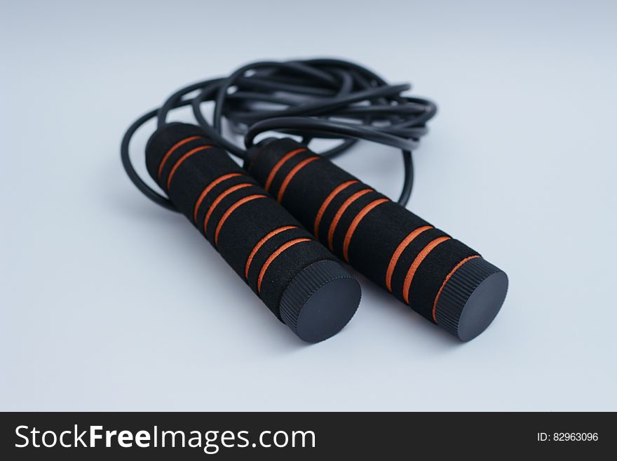 A jump rope with black handles with orange stripes.