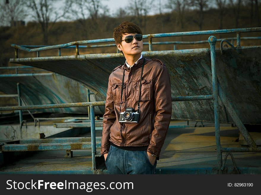 Outdoor portrait of man standing in leather jacket with camera around neck wearing sunglasses. Outdoor portrait of man standing in leather jacket with camera around neck wearing sunglasses.