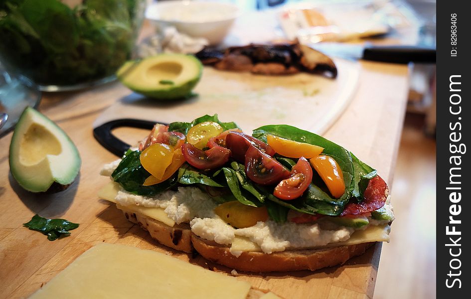 Close up of fresh vegetable sandwich with tomatoes and cheese on wooden cutting board with fresh avocado. Close up of fresh vegetable sandwich with tomatoes and cheese on wooden cutting board with fresh avocado.