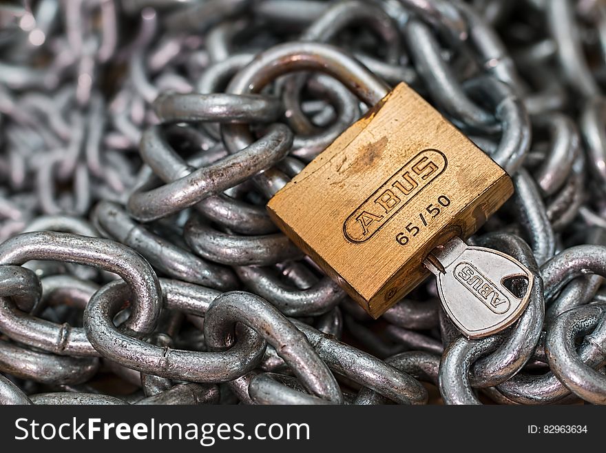 Brass padlock and key with selective focus and steel chain creating a background concept of security. Brass padlock and key with selective focus and steel chain creating a background concept of security.
