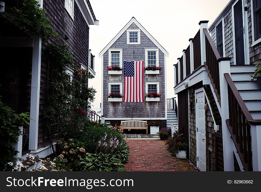 Courtyard of rustic old clapboard houses in America with the stars and stripes flag adorning the largest property. Courtyard is decorated with flowers and creepers. Courtyard of rustic old clapboard houses in America with the stars and stripes flag adorning the largest property. Courtyard is decorated with flowers and creepers.