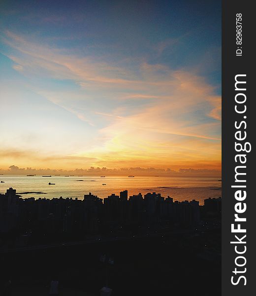 Sunset over silhouetted city skyline with sea in background.
