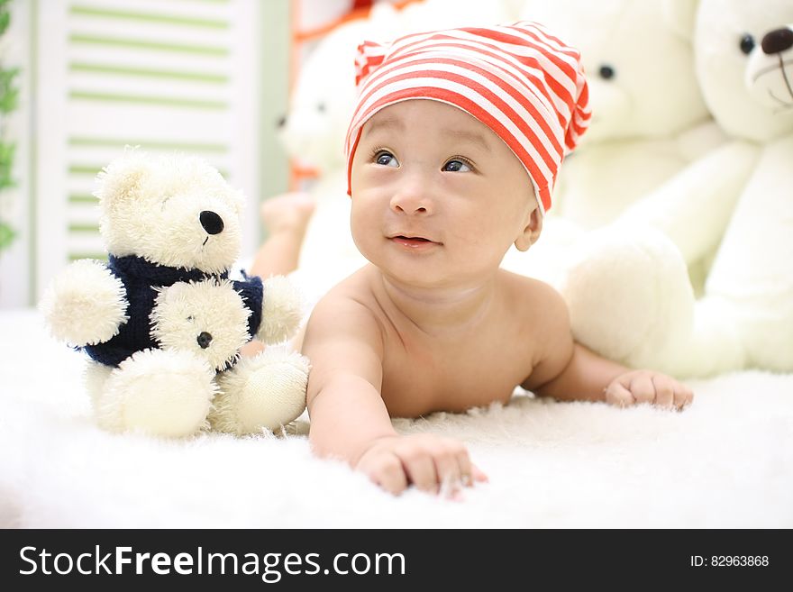 Smiling Toddler Wearing Orange and White Knit Cap Beside Black and White Bear Plush Toy