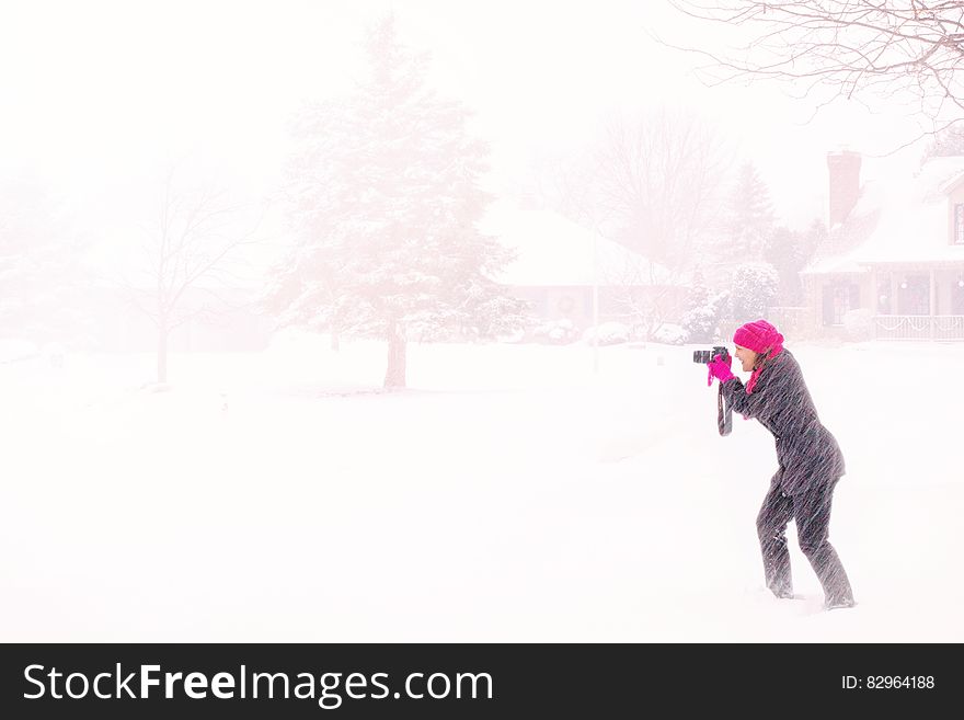 Woman in Pink Hijab Holding Black Dslr Camera Under Raging Snow during Daytime