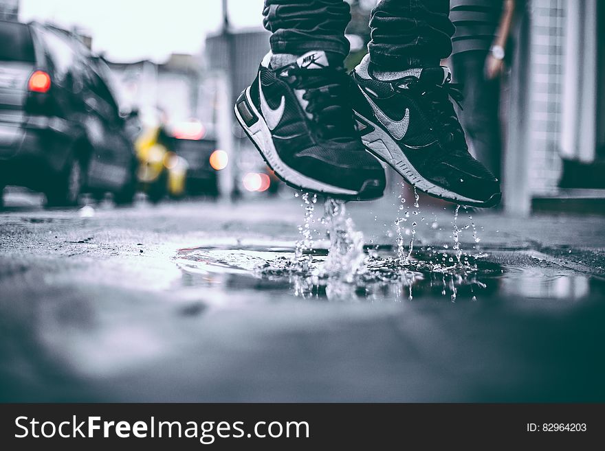 Feet wearing sneakers jumping in puddle on city streets. Feet wearing sneakers jumping in puddle on city streets.
