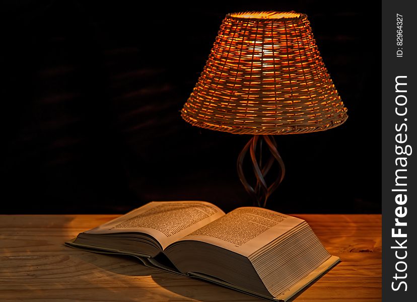 Open encyclopedia on wooden table under lamp with black background and copy space. Open encyclopedia on wooden table under lamp with black background and copy space.