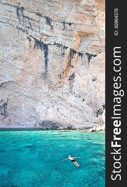 Man In Blue Waters Along Cliff