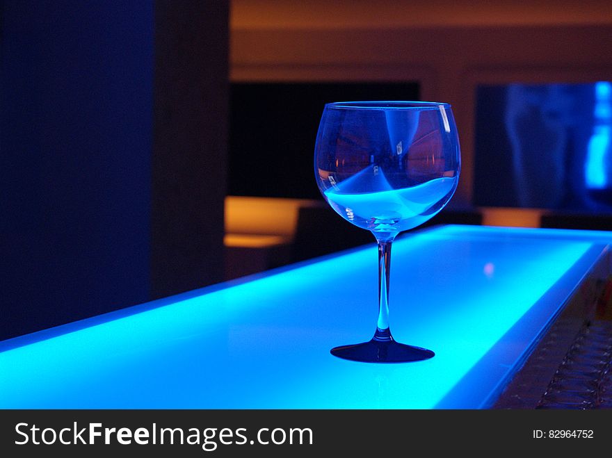 Stemmed glass on counter with blue light inside bar. Stemmed glass on counter with blue light inside bar.