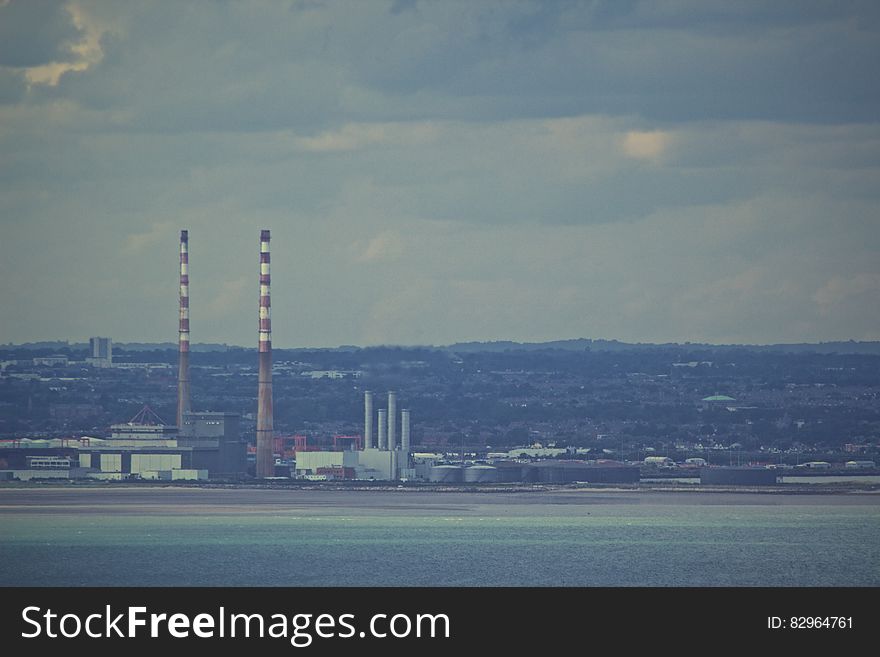 Factory smokestacks in factory on waterfront against cloudy skies. Factory smokestacks in factory on waterfront against cloudy skies.