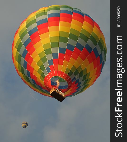 Colorful hot air balloon with basket against blue skies and white clouds.