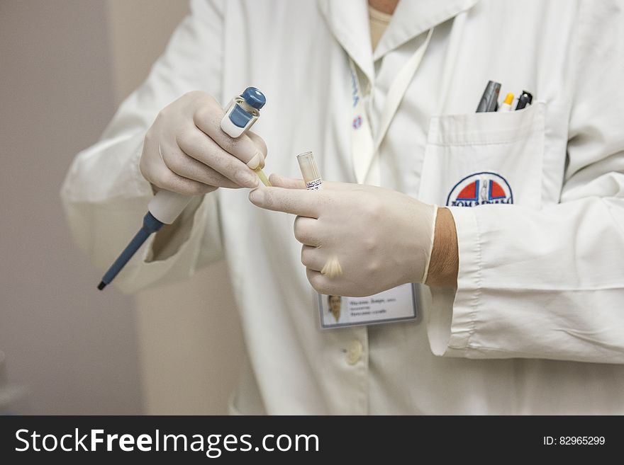 Clinician in white lab coat and gloves holding laboratory equipment. Clinician in white lab coat and gloves holding laboratory equipment.