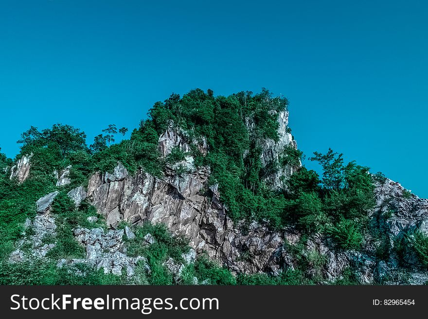 Tree covered rocky crag against blue skies on sunny day.