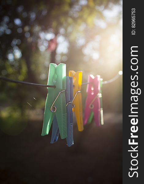 Closeup of green, blue, yellow and pink clothes pegs on a washing line with sunshine streaming through the trees in the background. Closeup of green, blue, yellow and pink clothes pegs on a washing line with sunshine streaming through the trees in the background.