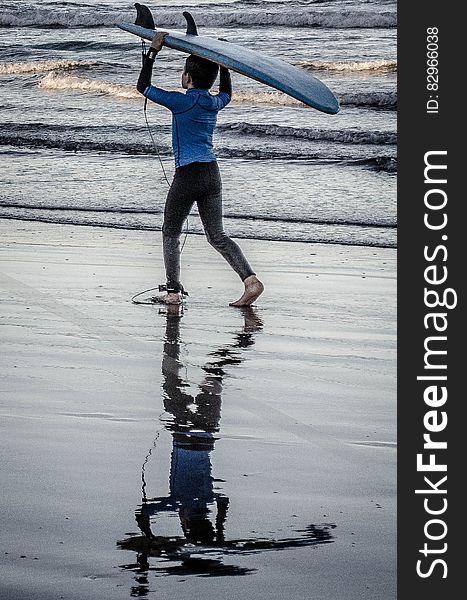 Young boy carrying surfboard along beach. Young boy carrying surfboard along beach.