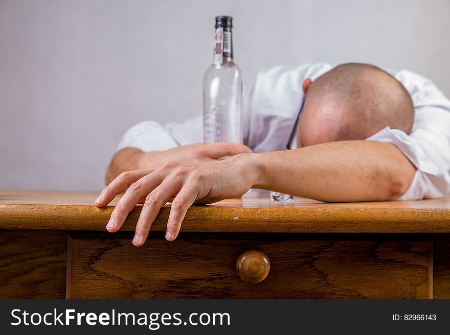 Man in White Dress Shirt Holding Glass Bottle on Brown Wooden Table