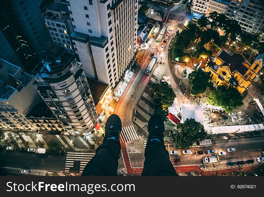 Man Sitting on High Rise Building Taking Photo Below