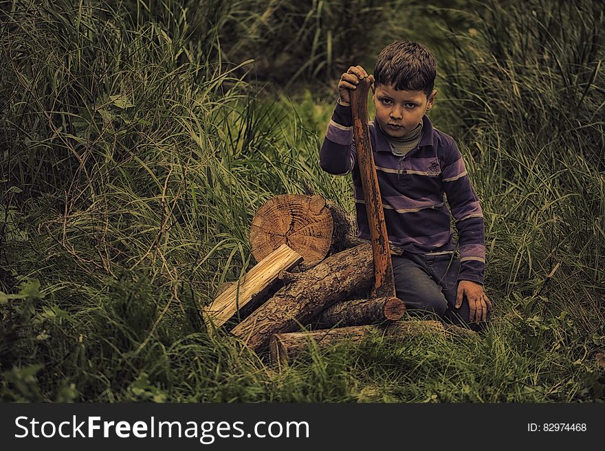 Boy In Purple Stripe Print Long Sleeve Shirt Holding Wooden Rod On Green Grass Field