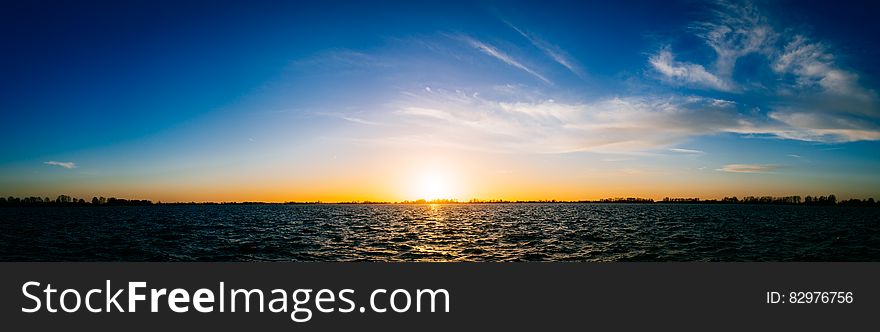 Panoramic horizon of sun set over lake with blue and orange skies. Panoramic horizon of sun set over lake with blue and orange skies.