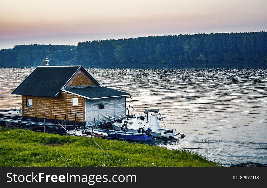 White Boat Beside Wooden House on Water Near Forest