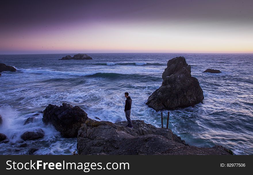 Man In Black Shirt Standing On Rock In Between Sea Water