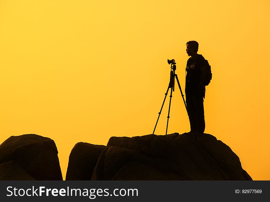 Silhouette of photographer of rocky crag against yellow skies at sunset.